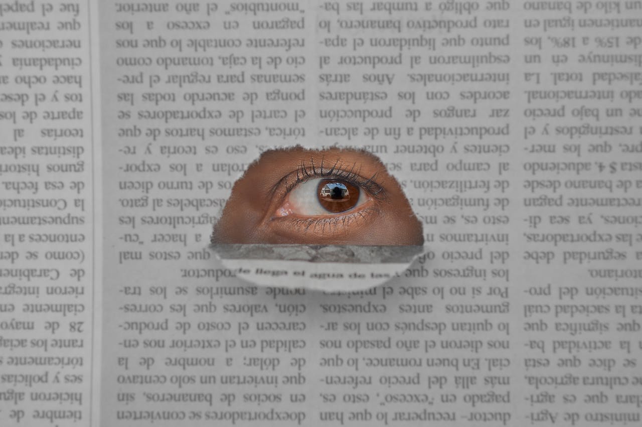 Artistic image of an eye peering through a hole in a newspaper, symbolizing insight and observation.